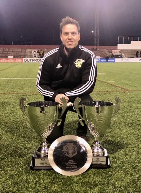 Sam Ellis-Stockley poses with several trophies the Detroit City FC won. Ellis-Stockely is on the Medical Team and assists the team with medical needs.