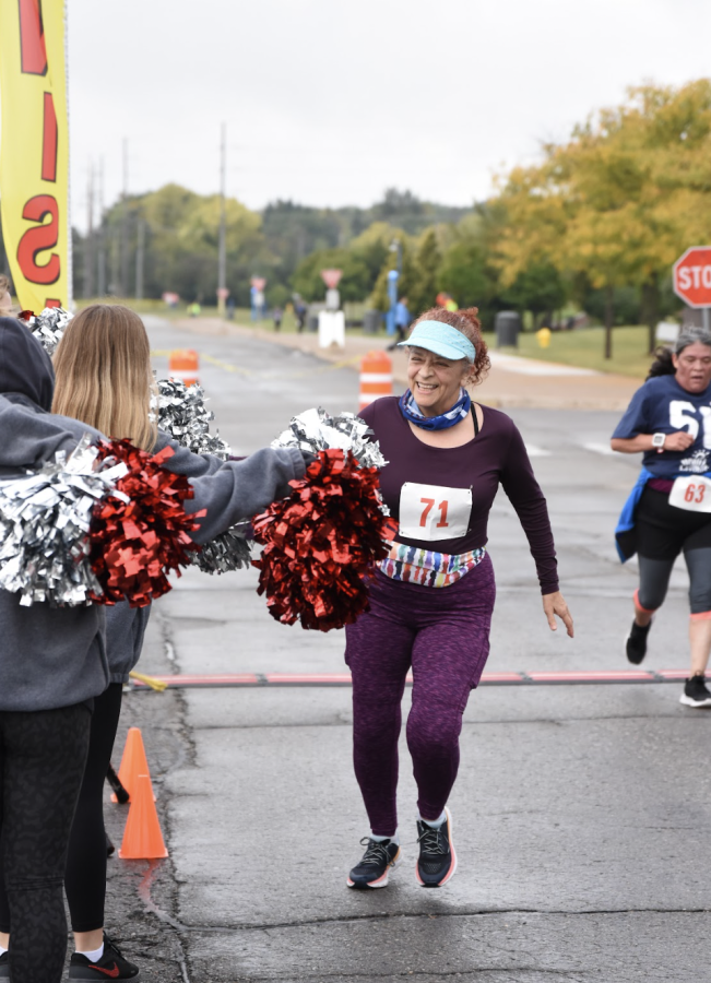 A participant of the Healthy Livonia 5k crosses the finish line and is greeted by the cheerleaders. The 5k was held on the campus of Schoolcraft College on Sunday, September 25, 2022.