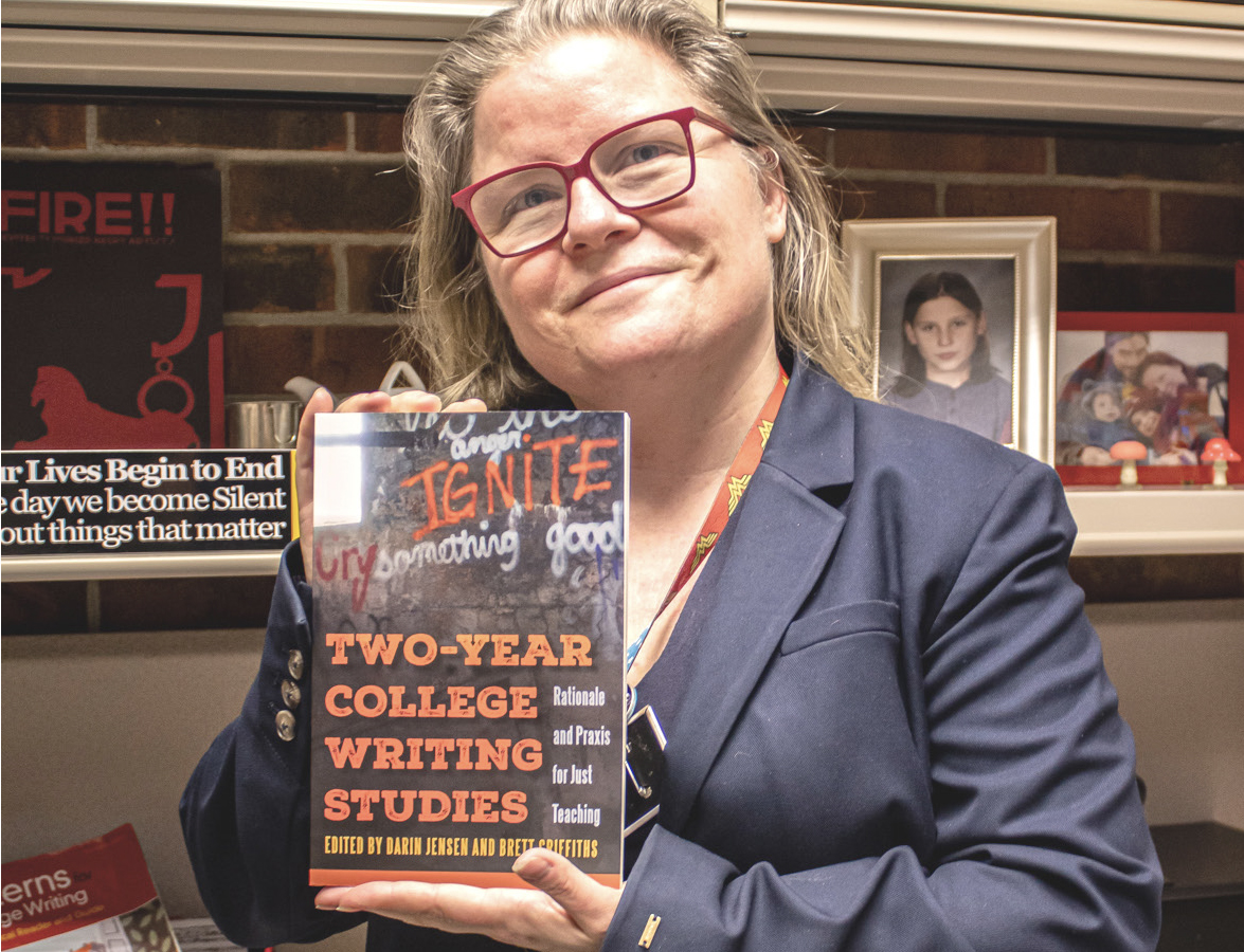Professor Brett Griffiths holding her book “Two-Year College Writing Studies” in her office.