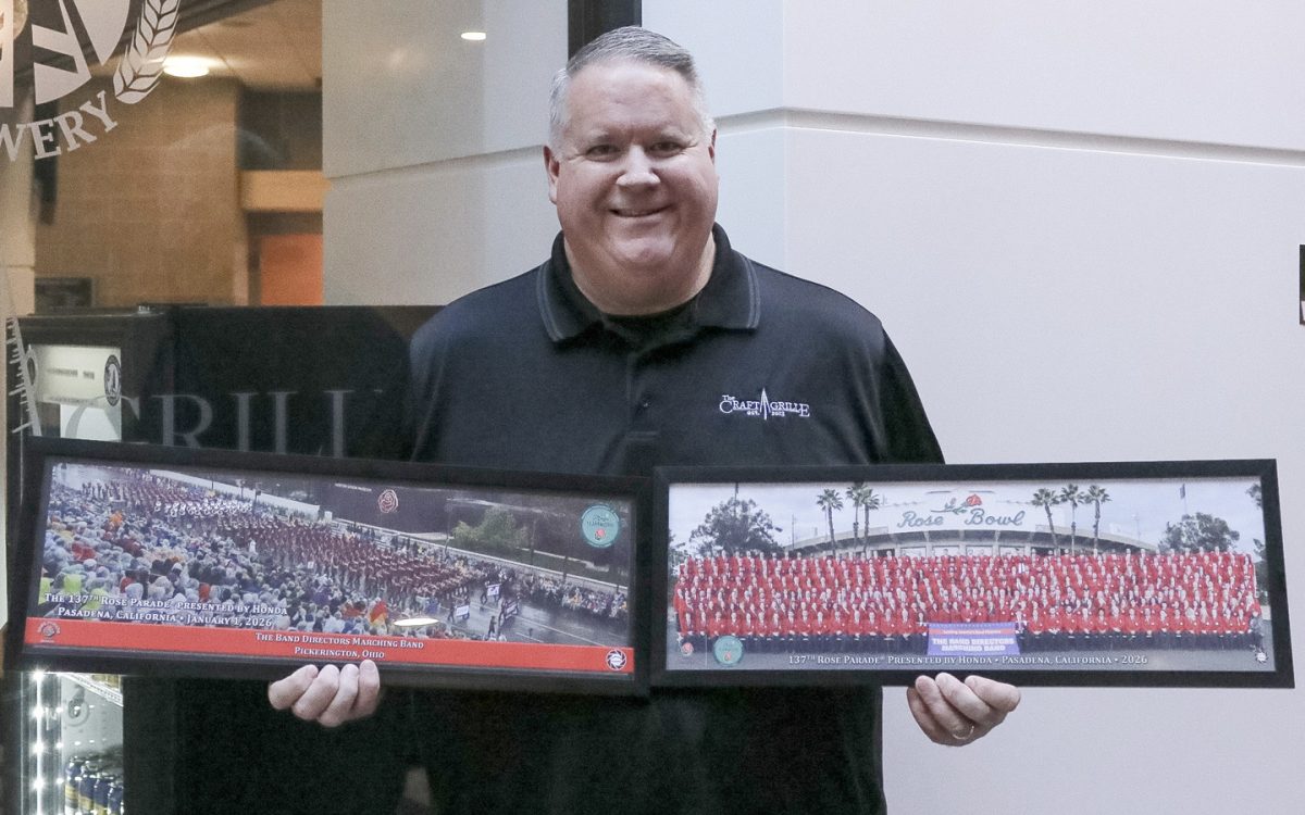 Jeff Groth, manager of The Craft Grille poses with panoramic photos from his performance in the Rose Bowl Parade.